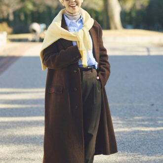 コートの上からバナナイエローのニットを肩かけ