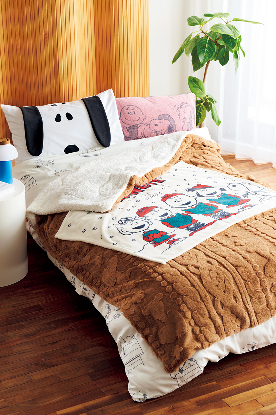 （ベッドに重ねたアイテム、下から）綿100％のサテン生地で肌ざわり滑らか。掛けふとんカバー（シングルロング：150×210cm）￥8,800。 表はスヌーピーのシルエットを織りで柄を描いた素敵なフェイクファー、裏はふんわりシープボアであったか！　キルトケット（シングル：140×200cm）¥9,900。洗えるので屋外でも使えるオケージョンひざ掛け（100×70cm）￥1, 980。（右上）のびのびタオルピローケース（約64×34cm）￥2, 200、（左上）ピローケース（65×45cm）￥2,970／すべてnishikawa